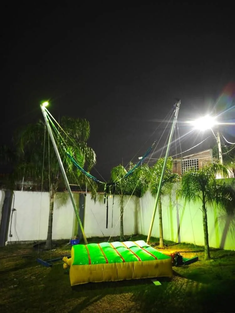 Eurobungy de Papus instalado en un jardín de noche, con arnés, postes y base inflable verde y amarilla